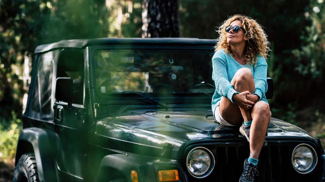 Middle aged woman sitting on top of hre jeep.