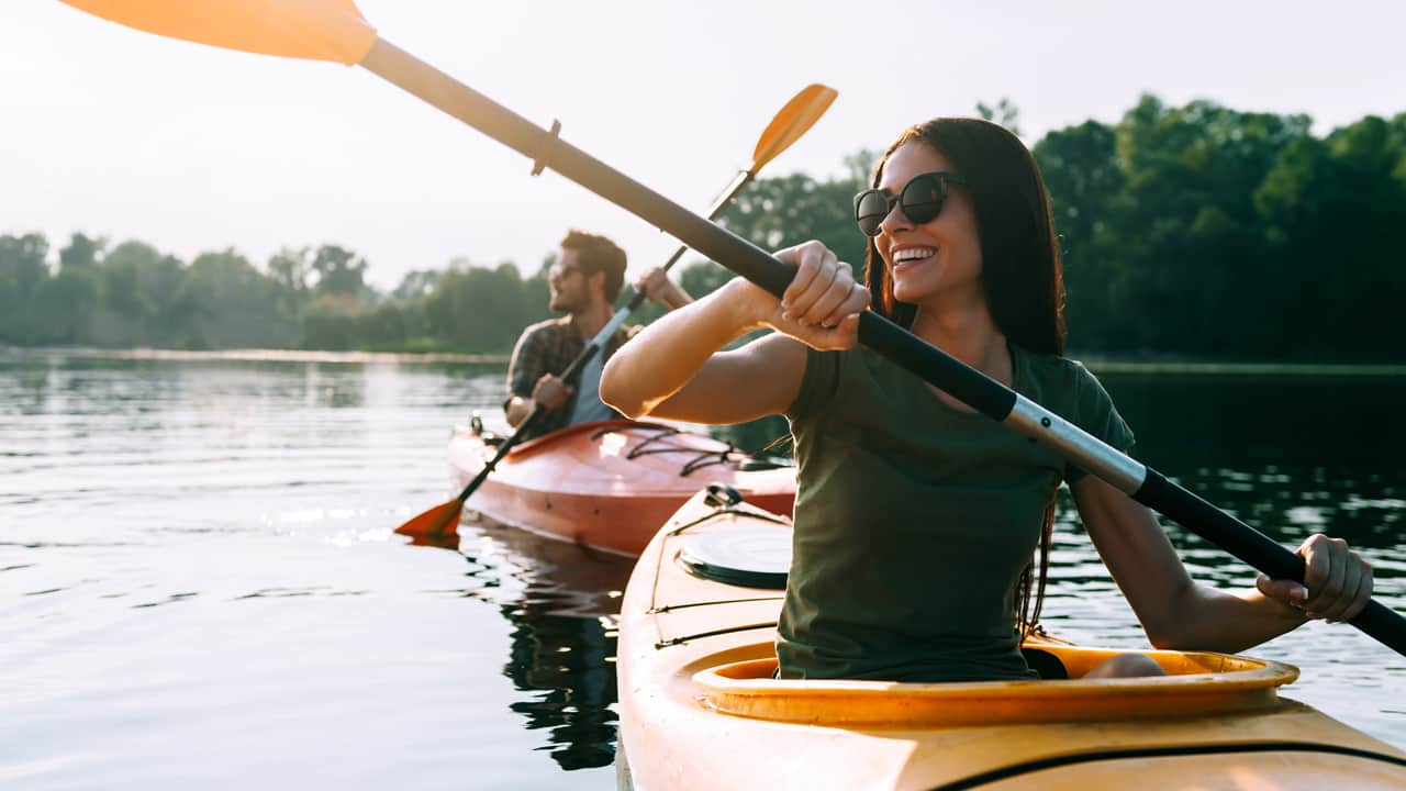 Girl and guy in kayak in a lake surrounded by green trees.