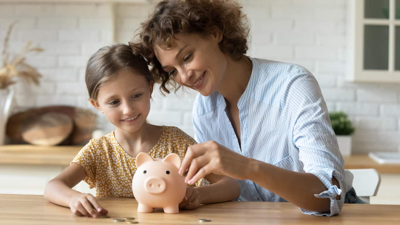 Grandmother and grand child at kitchen table putting money in biggy bank.