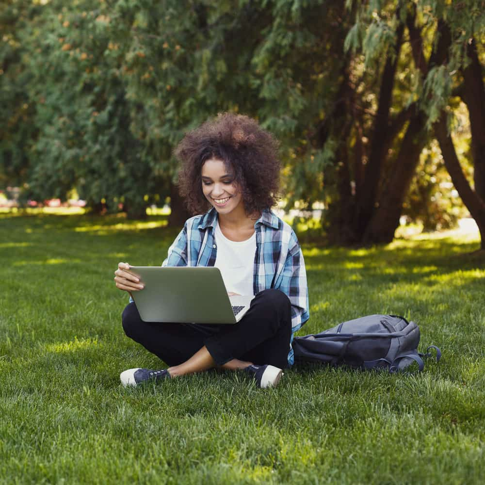 Girl sitting on campus lawn looking at laptop