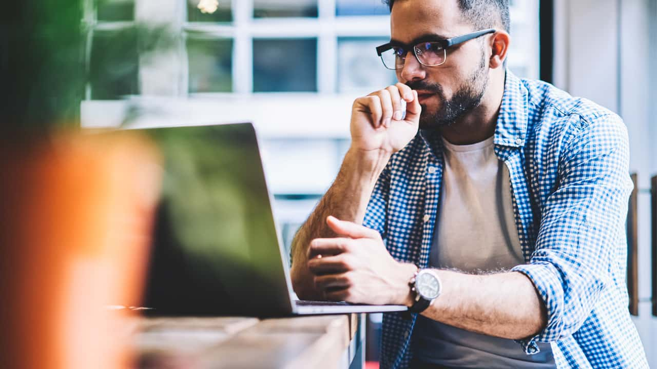 Man using his laptop. He's wearing a blue checkered shirt.